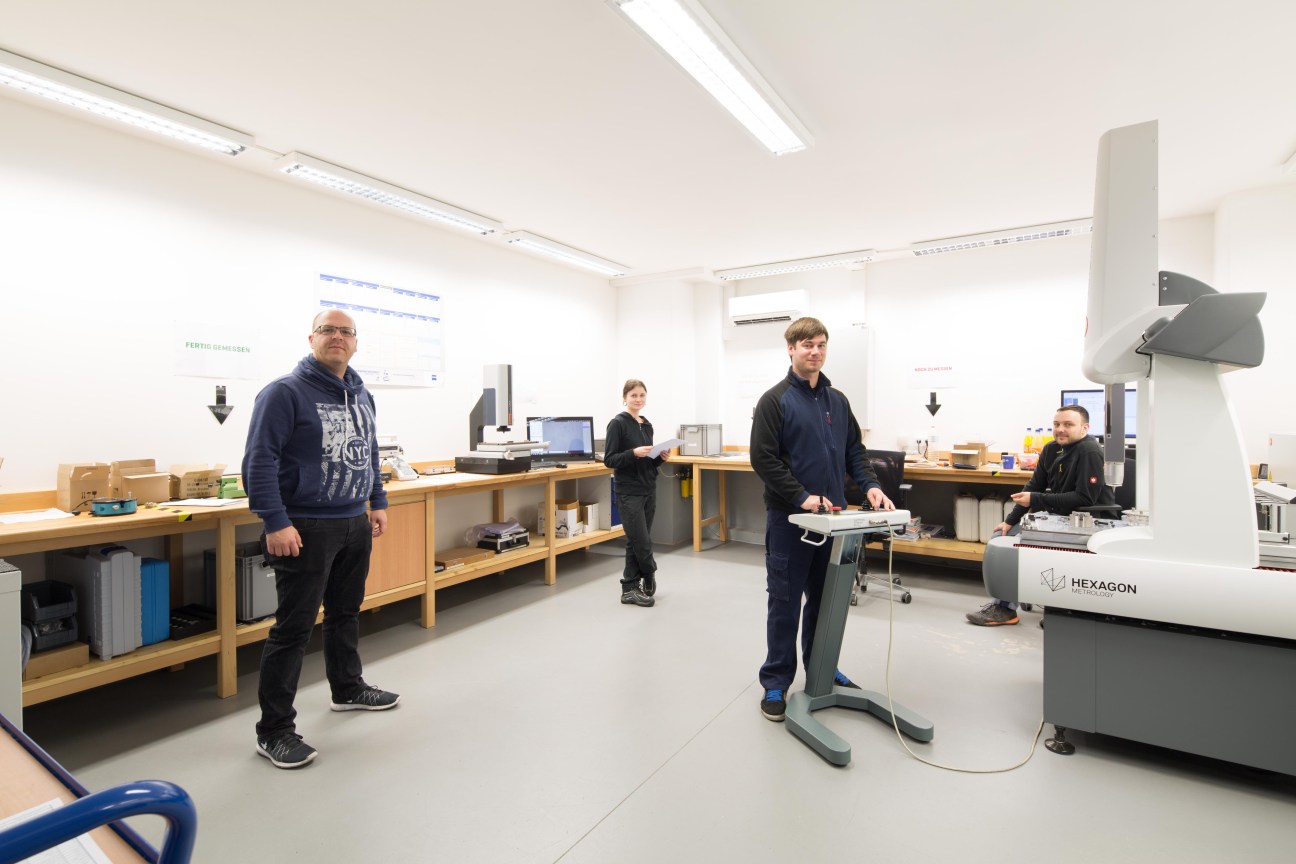 Industrial laboratory with staff working at workstations equipped with precision measurement tools and microscopes.