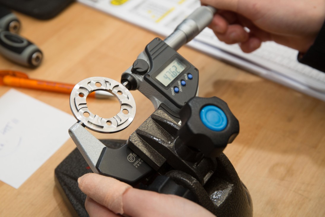 Kappstein employee measuring a precision metal bike component with a digital micrometer on a workbench.