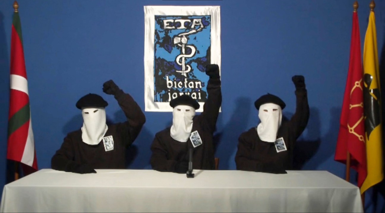 Three members of Basque separatist group ETA at a press conference holding the group's flag and logo behind them.