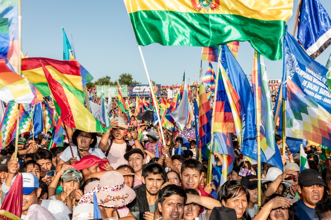 Large crowd of Bolivian supporters waving colorful flags at outdoor political rally