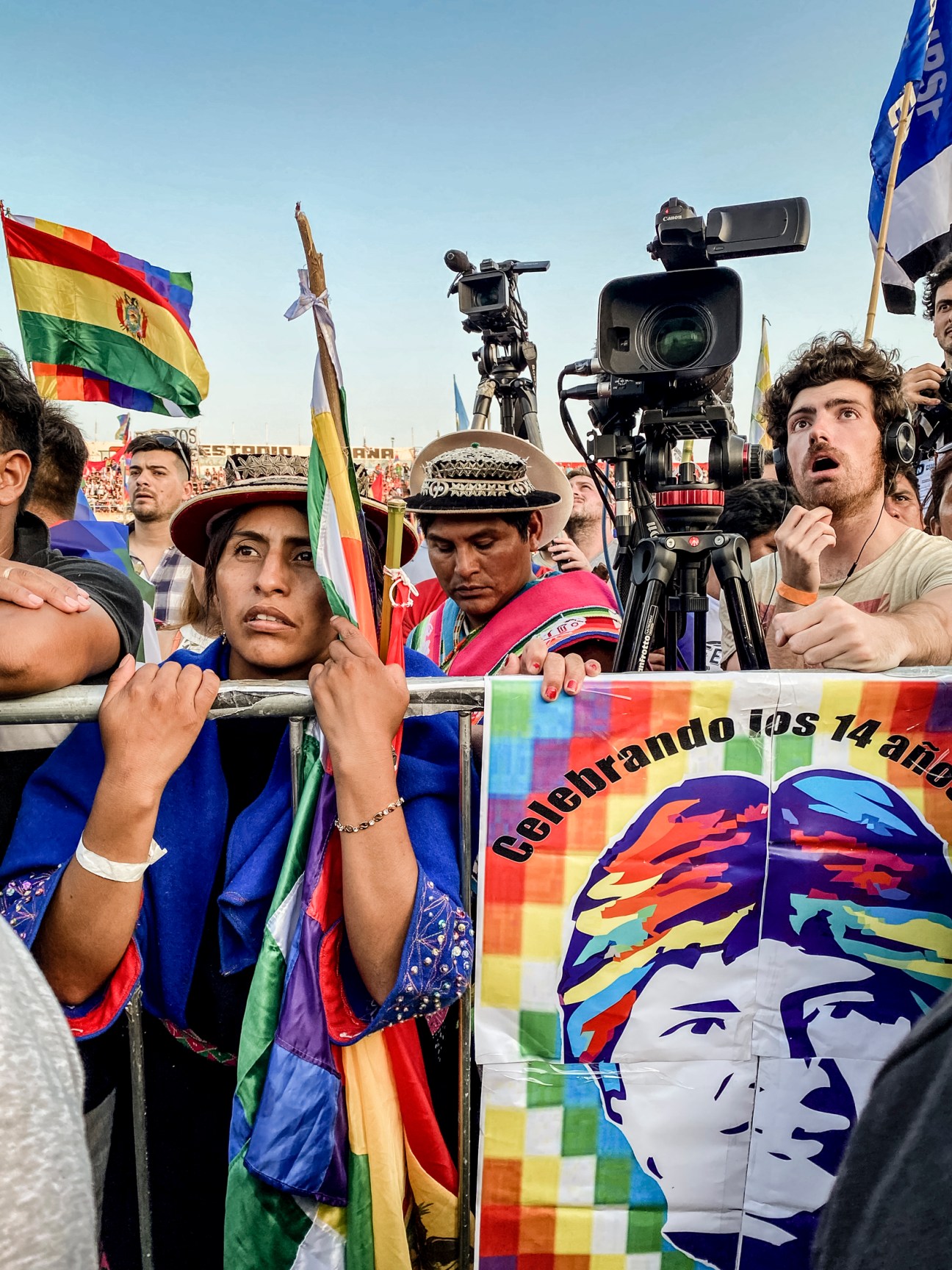 Supporters at rally holding colorful poster celebrating Evo Morales with text referencing his 14 years in power