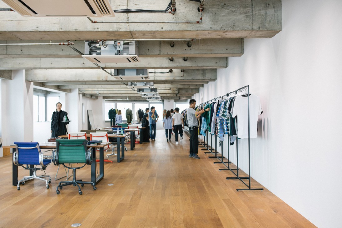Sacai Studio in Aoyama featuring exposed concrete ceiling, wooden floors, clothing racks, and staff working in an open industrial space.