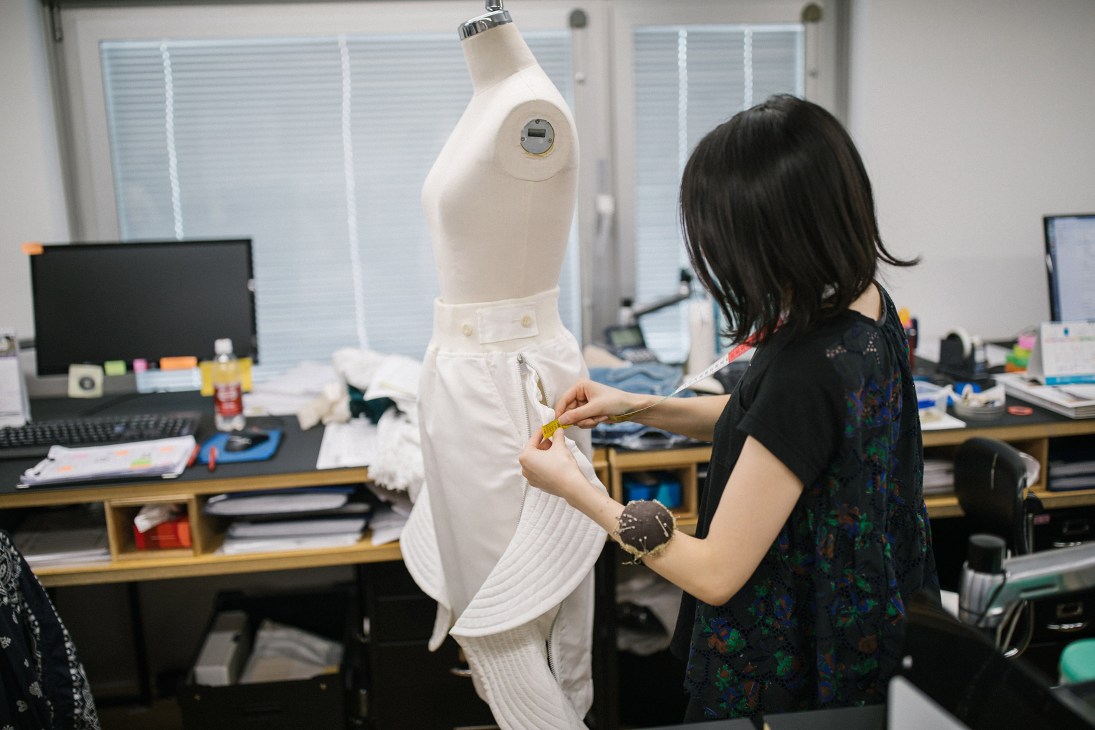 Designer adjusting a white garment on a dress form in Sacai's studio workspace.