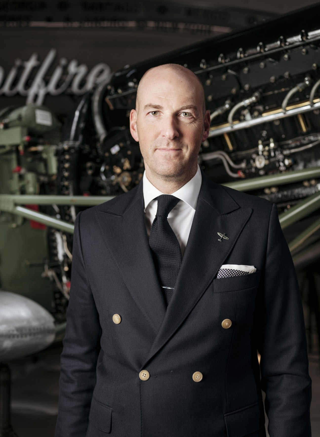 Wilhelm Schmid, CEO of A Lange & Söhne, in formal business attire standing before aircraft engine machinery.