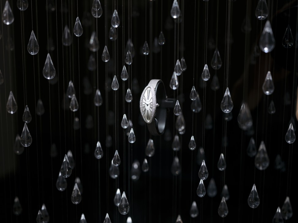Cartier's Baignoire Allongée watch displayed among hanging crystal teardrop decorations against a dark background.