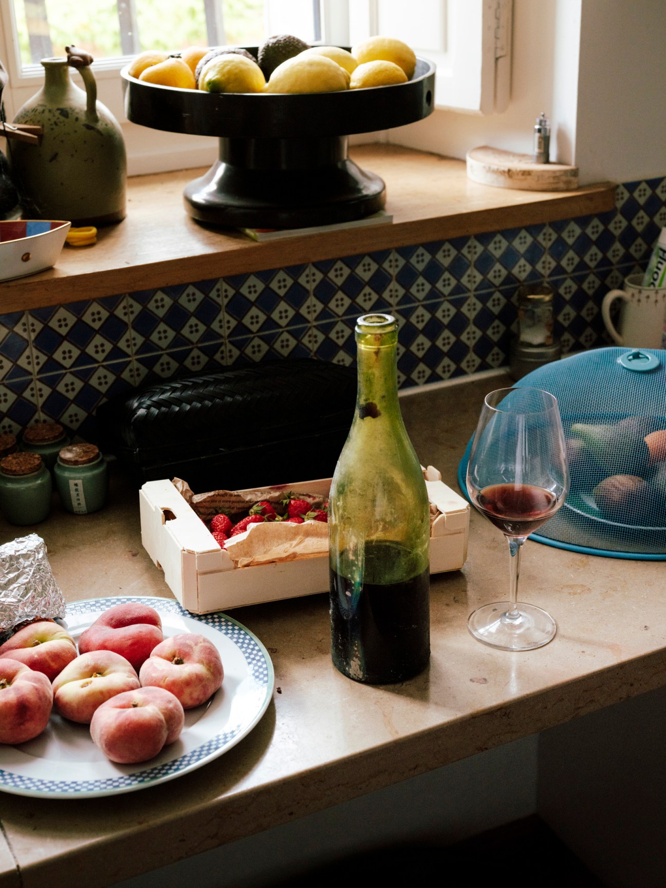 Kitchen counter at Domaine Dujac with wine bottle, glass, fresh fruit, and black pedestal bowl.