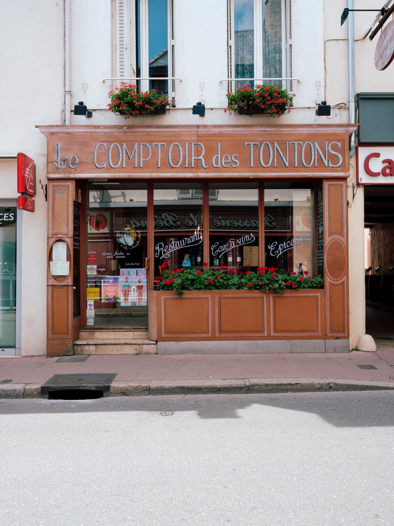 Le Comptoir des Tontons, a traditional French wine shop with wooden facade and red flowers in Beaune.