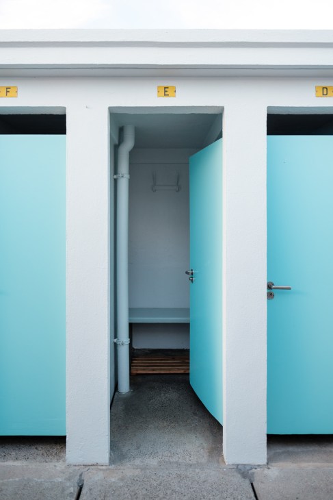 An open private changing room at Bains des Pâquis with turquoise door and white walls.