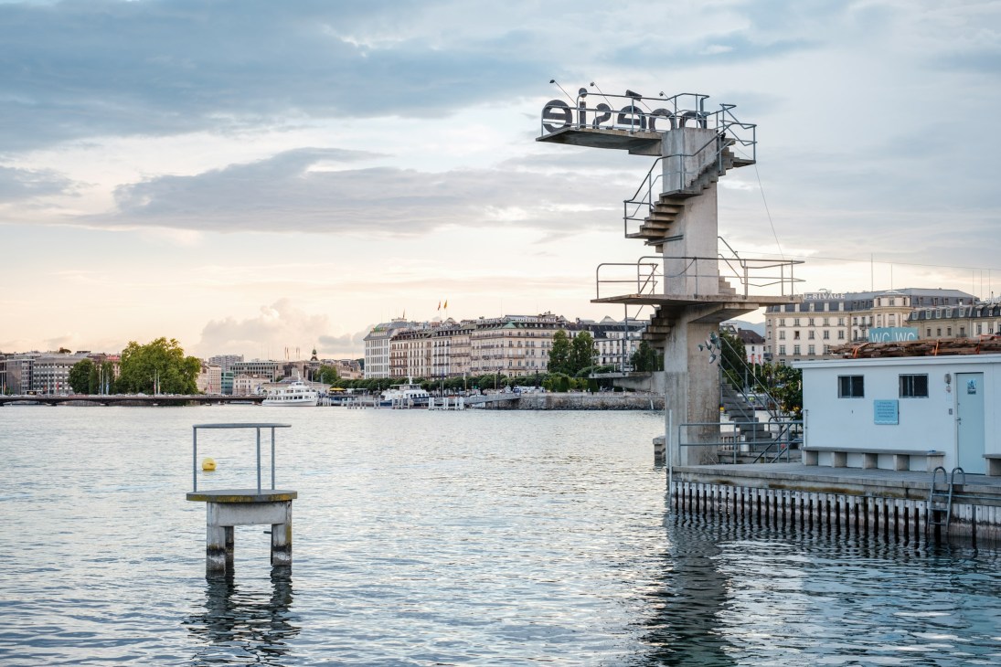Three-tier diving platform with red 'poésie' lettering overlooking Lake Geneva and the old town of Geneva.