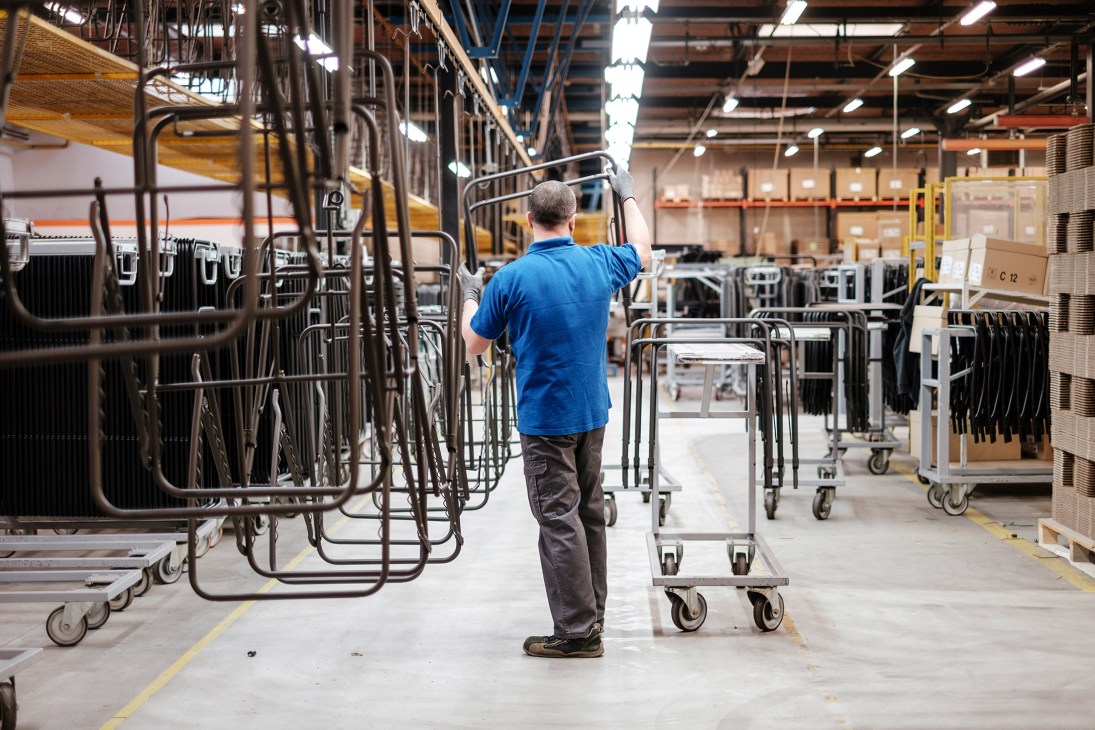 Worker in blue shirt inspecting stacked metal chair frames in Lafuma Mobilier's production facility.