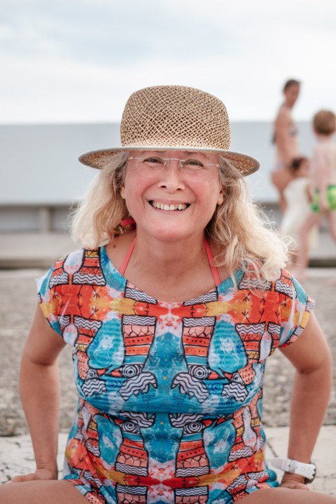 Woman in straw hat and colorful patterned swimsuit smiling at the Bains des Pâquis beach.