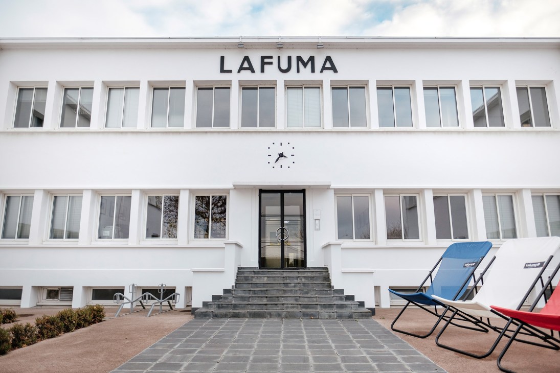 Lafuma Mobilier's white headquarters building with large windows, entrance stairs, and folding chairs displayed on the paved forecourt.
