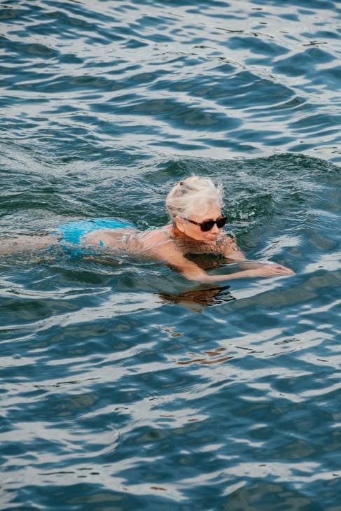 An older woman with white hair and sunglasses swimming in Lake Geneva.