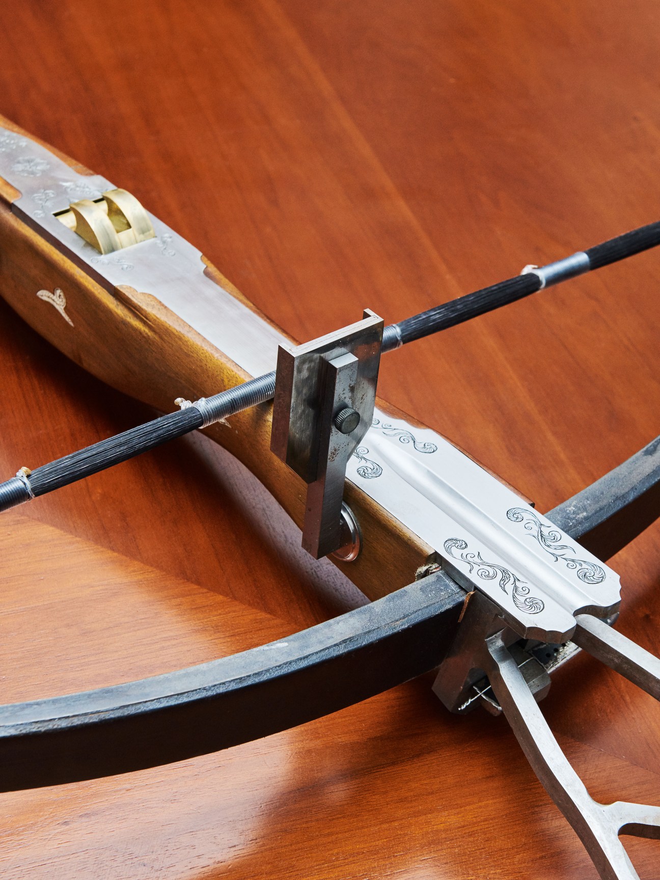 Ornate crossbows with decorated wooden stocks and metal mechanisms displayed against a red-brown fabric backdrop.