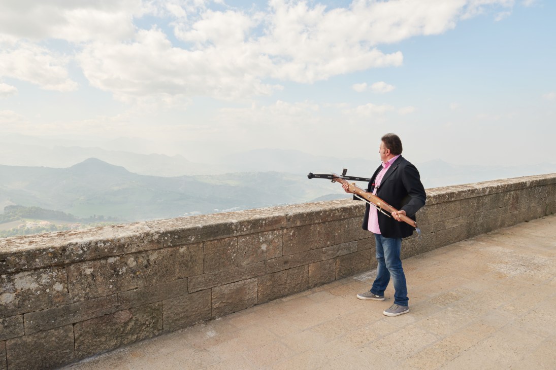 Stefano Ugolini, chairman of the Crossbow Corps, aims a rifle while standing on ancient fortification walls overlooking San Marino's landscape.