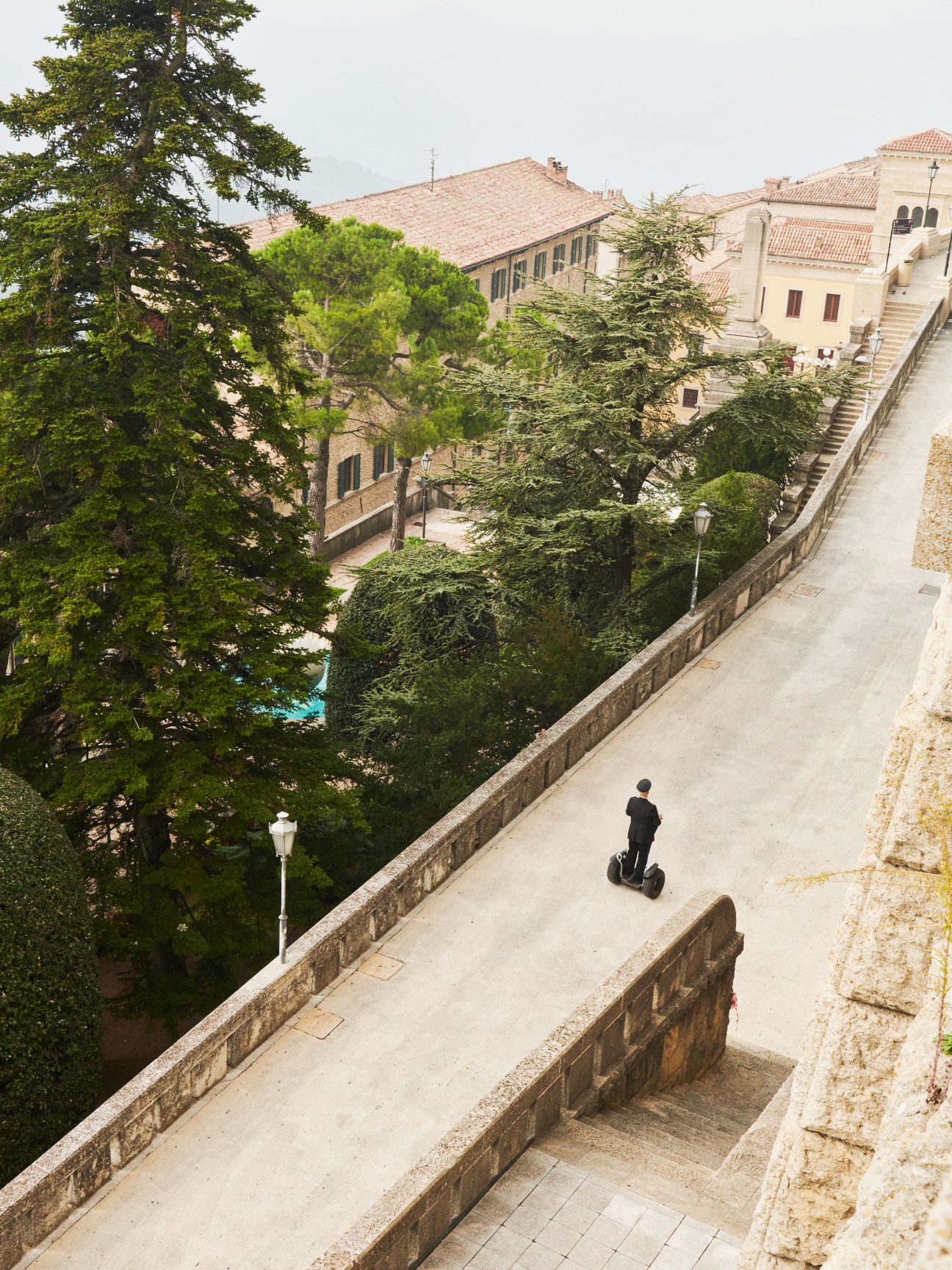 A Gendarmerie officer on a Segway rides along a stone-walled path above San Marino's historic architecture.