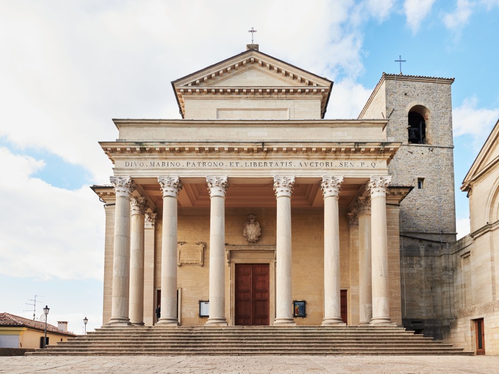 Neoclassical basilica with white stone columns, pediment, and bell tower under blue sky