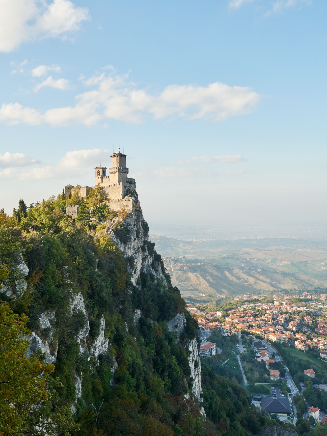 Medieval Guaita fortress perched on a rocky cliff with towers overlooking San Marino's landscape below.