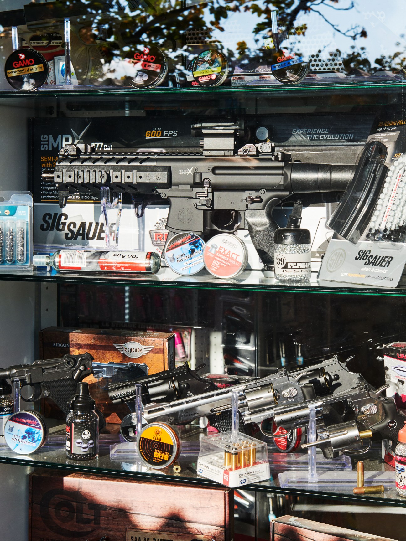 Display case with air rifles, ammunition, and replica firearms for sale.