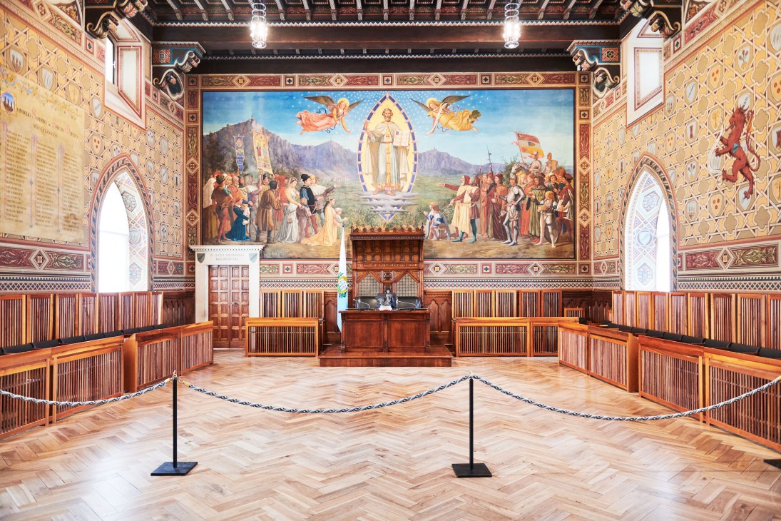Grand and General Council meeting room inside Palazzo Pubblico with ornate frescoed walls and wooden benches.