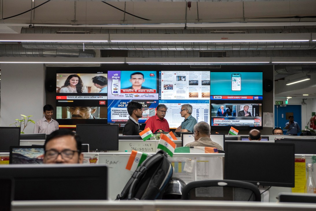 Times of India newsroom in New Delhi with staff at desks, Indian flags, and multiple TV screens displaying news.