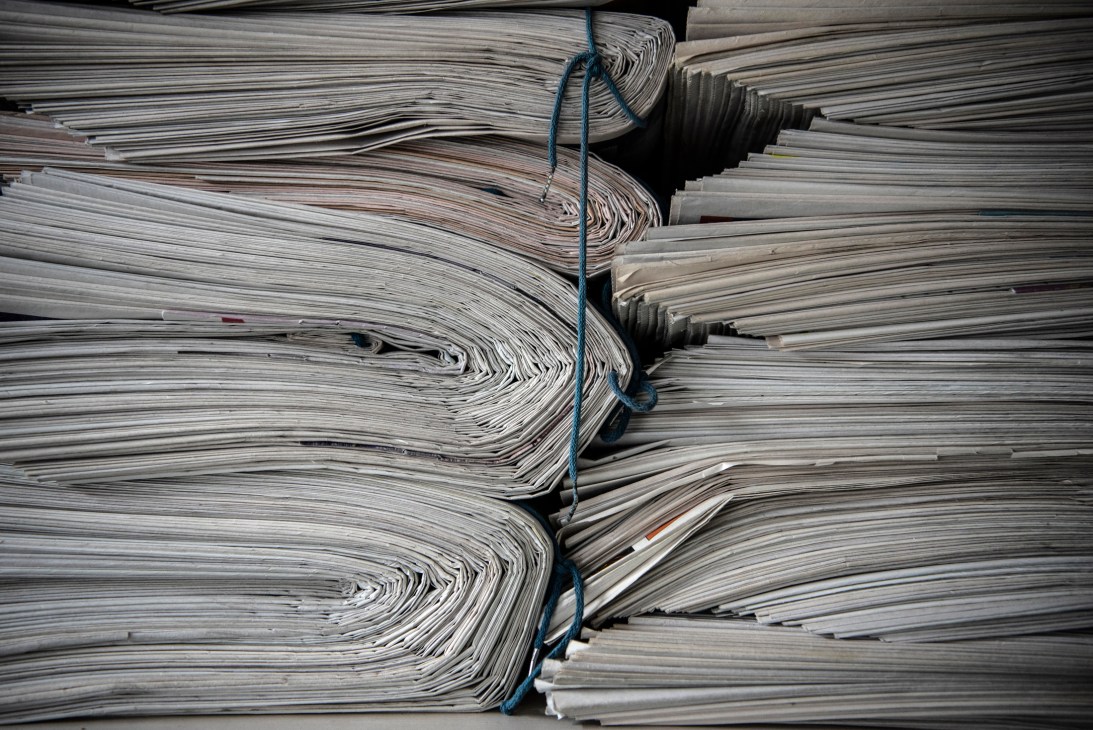 Bundles of newspapers tied with blue string stacked and ready for delivery.