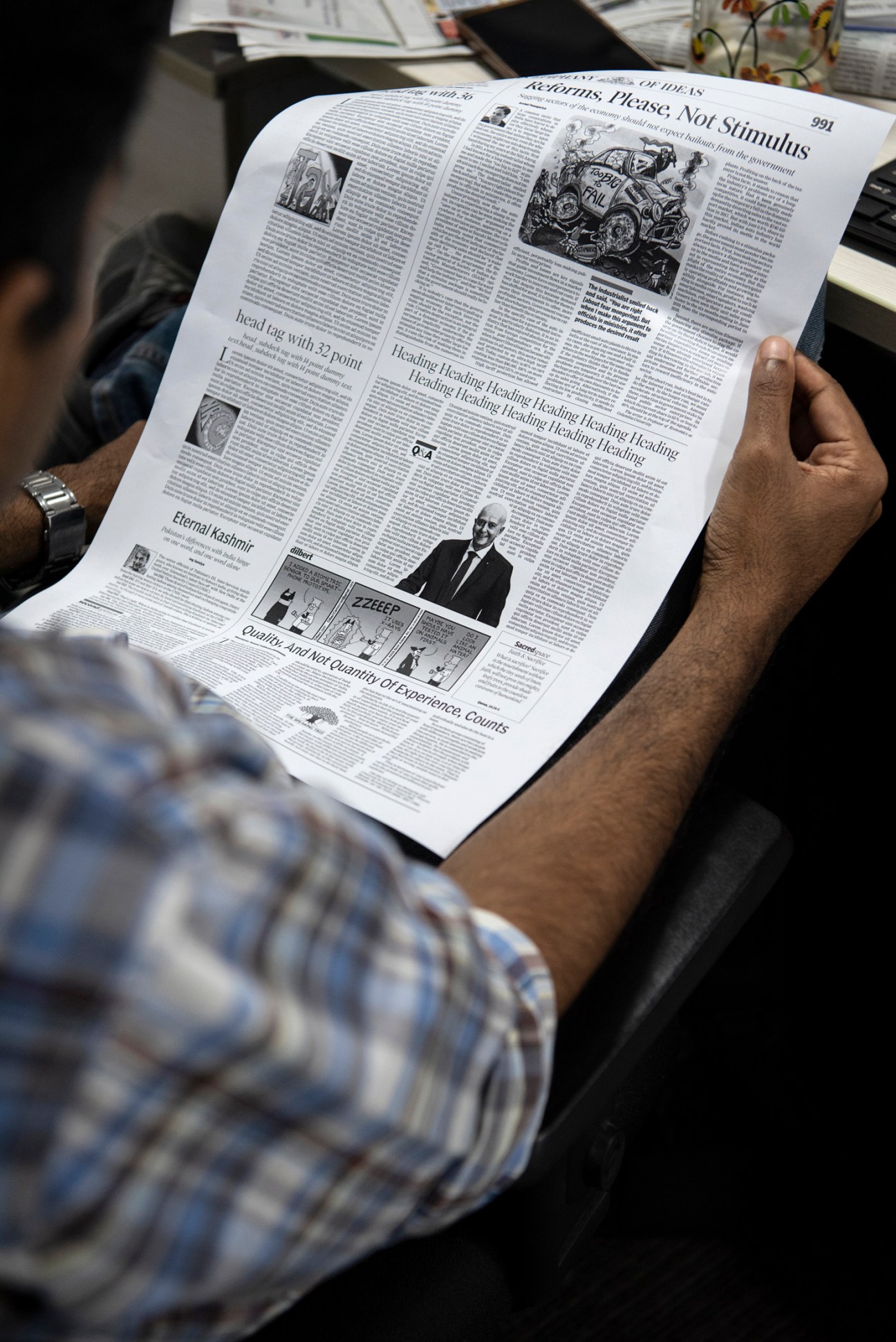 Person holding open a newspaper page showing multiple articles and illustrations.