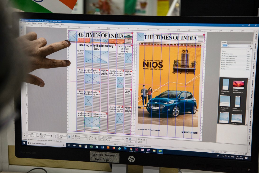 Hand pointing at Times of India newspaper layout on computer screen showing design templates and advertisement placement.