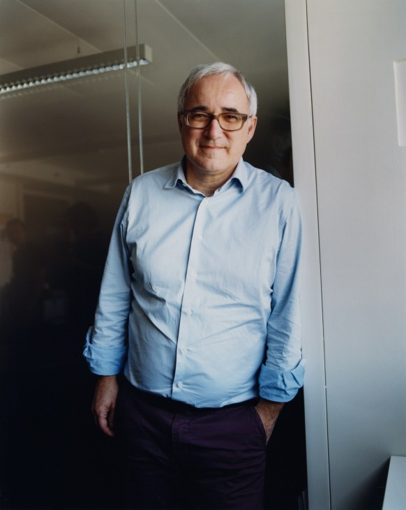 Franceinfo director Vincent Giret stands in a modern office hallway wearing a light blue shirt and glasses.