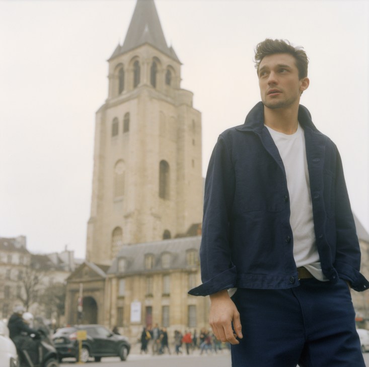 Man in navy jacket and trousers standing in front of a church tower in Paris.