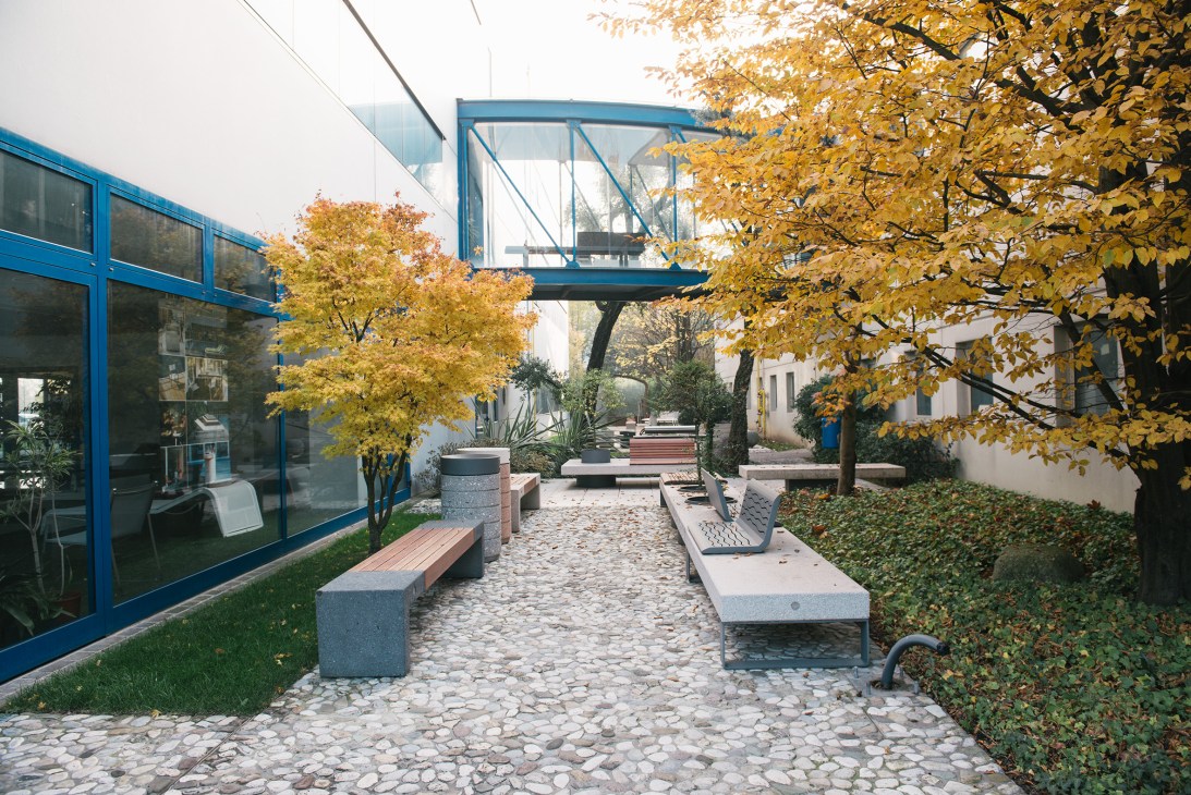 Metalco's outdoor showroom courtyard with modern benches, autumn trees, and blue-framed building.