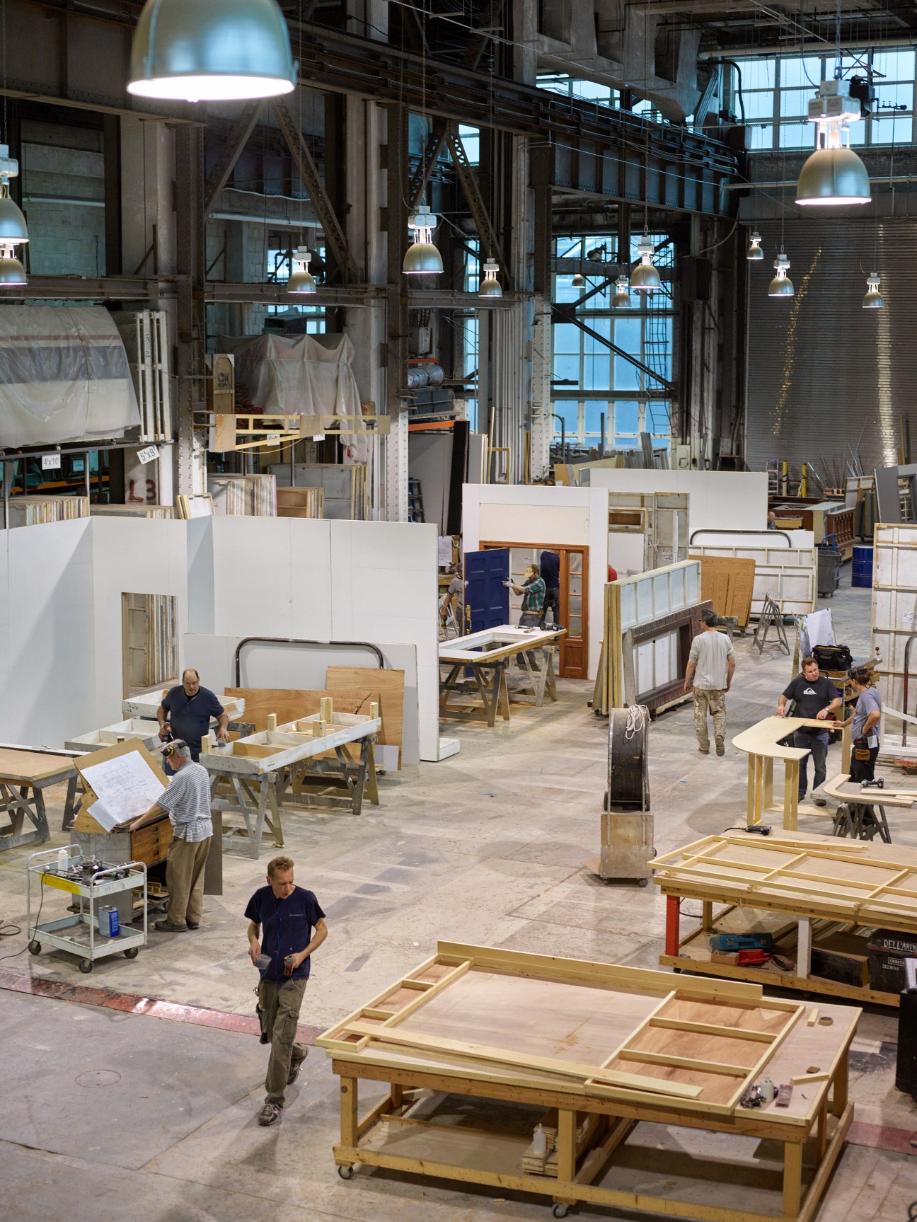 Workers construct television set pieces in a large industrial hangar at Stiegelbauer Associates' scenic shop in Brooklyn Navy Yard.