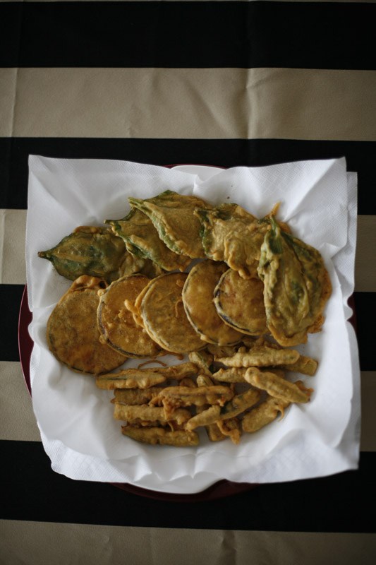 Deep-fried pakoras of spinach, aubergine and okra served on white paper.