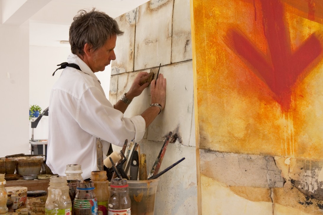 Italian artist Paolo Maria works on a canvas with orange and red tones in a studio setting.