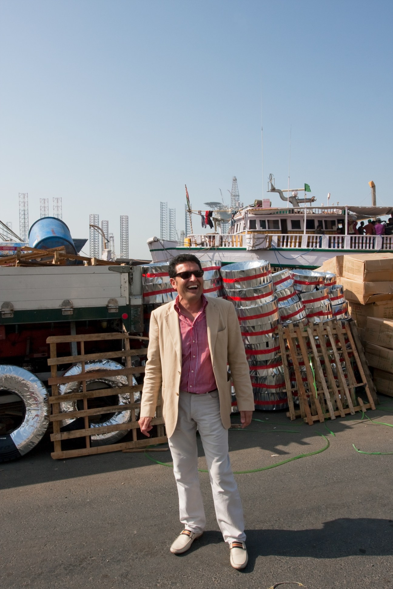 Jack Persekian, director of the Sharjah Biennial, stands at a port surrounded by cargo, boats and shipping containers.