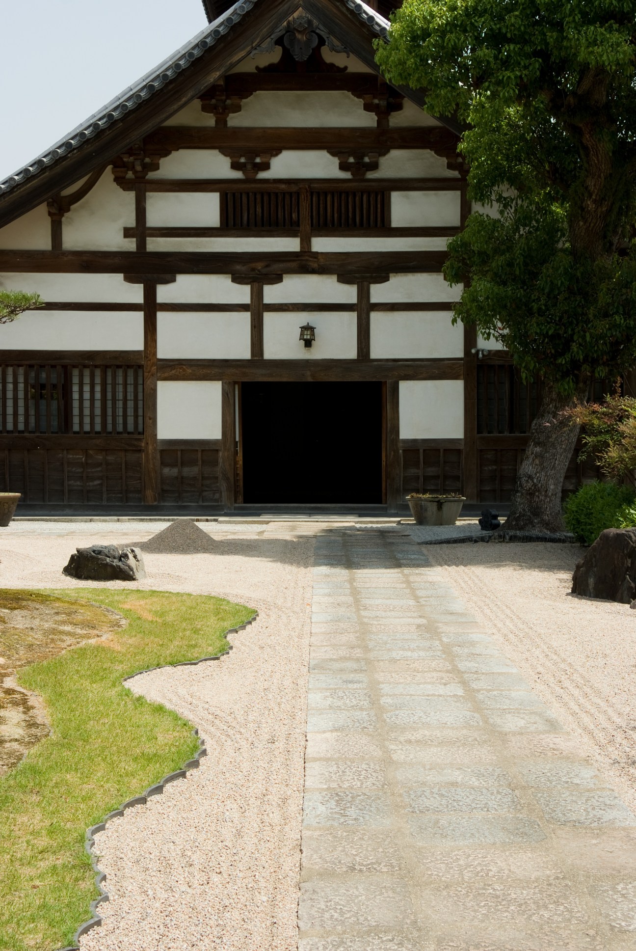 Traditional Japanese temple building with dark wooden beams, white walls, and a manicured gravel courtyard.