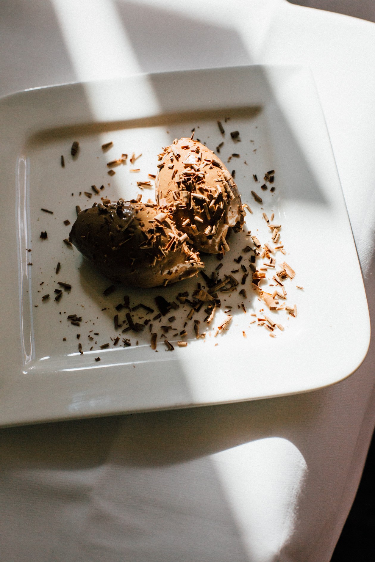 Mousse au chocolat dessert garnished with chocolate shavings on a white square plate.