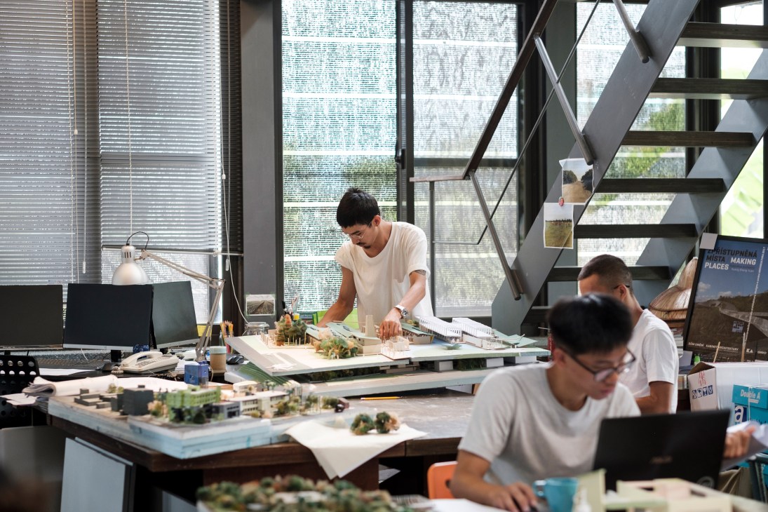 Architects working on scale models and drawings at drafting tables in a modern studio with stairs