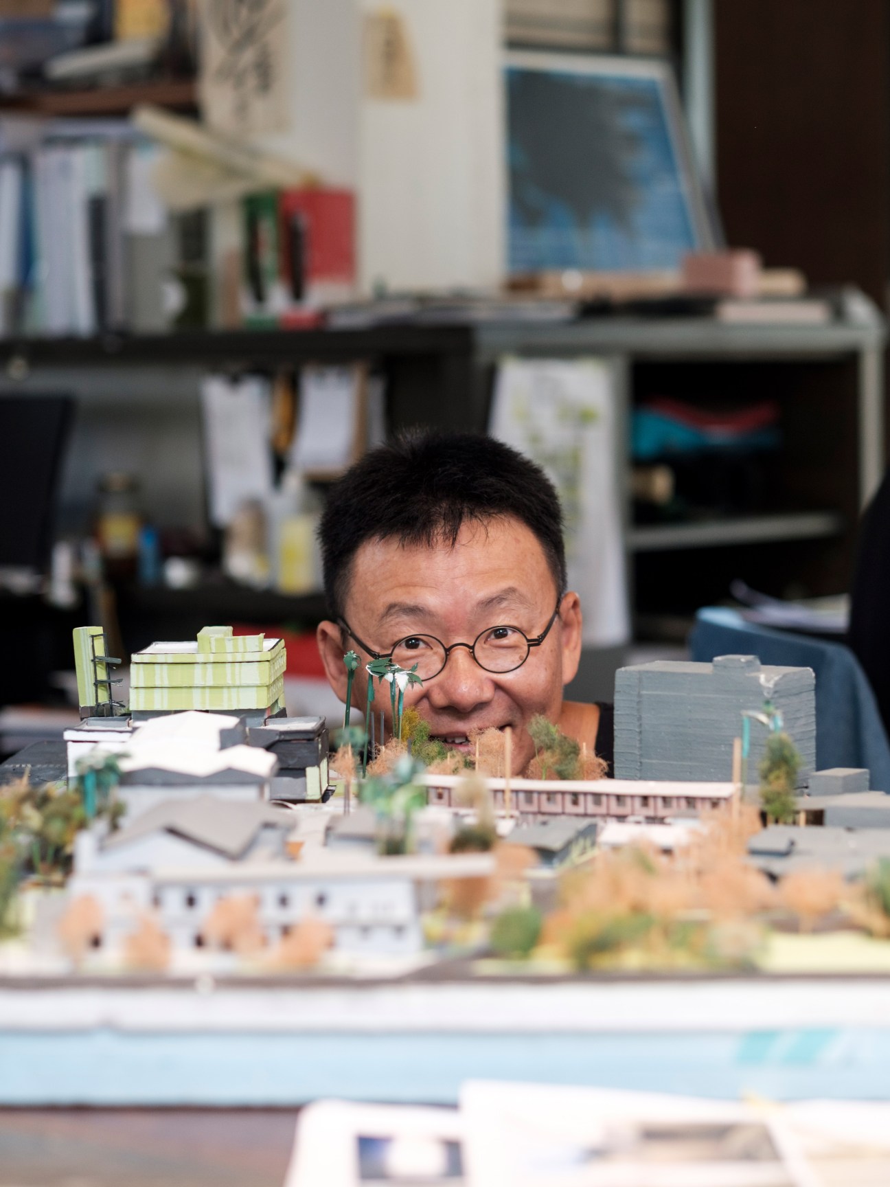 Huang Sheng-yuan smiling behind an architectural model in his office