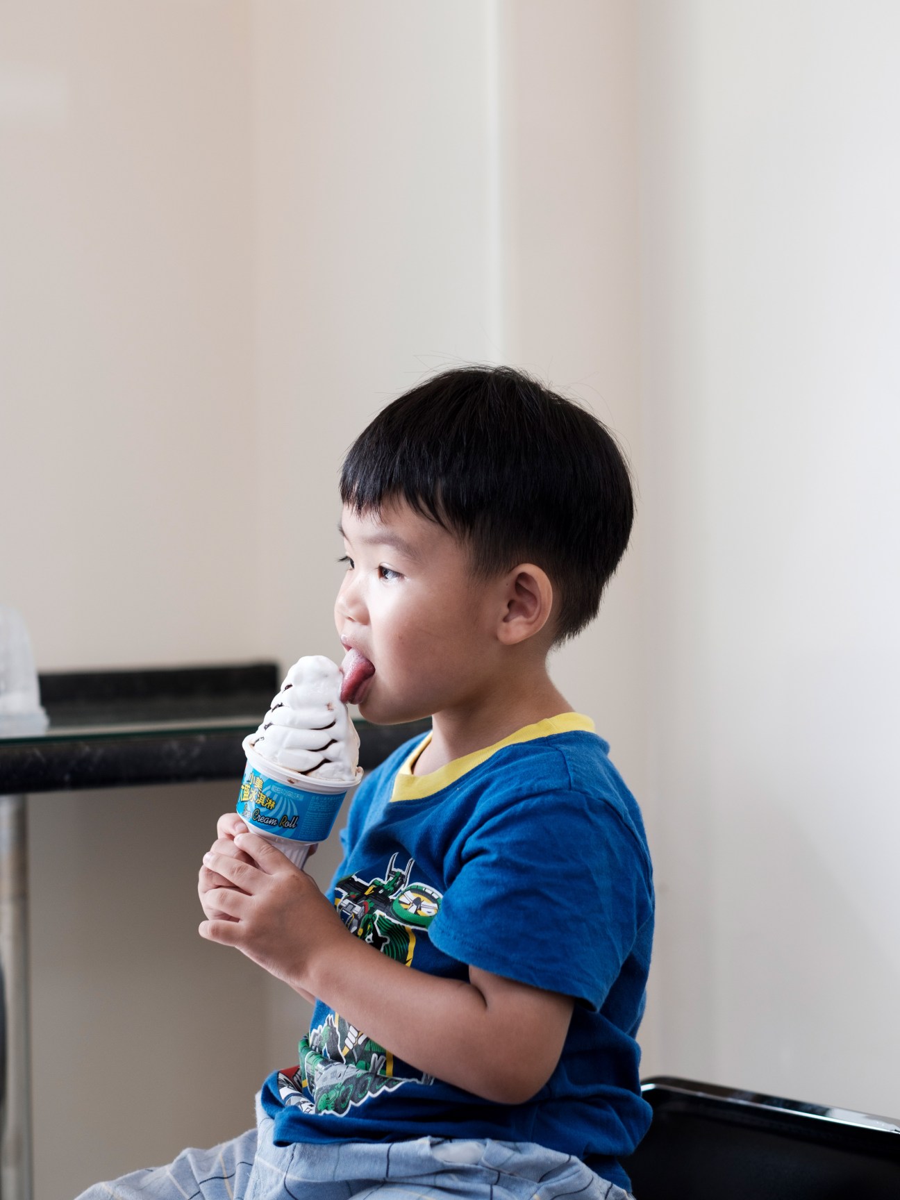 Young boy in blue shirt eating white soft-serve ice cream cone indoors