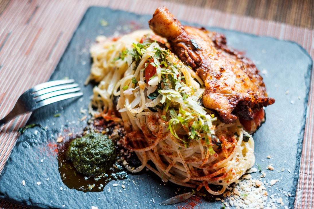 Grilled chicken drumstick with noodles and green sauce on dark slate plate