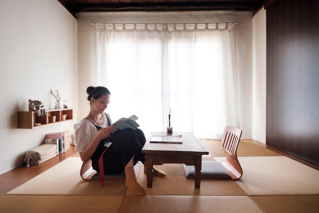 Woman reading book while sitting cross-legged on tatami mat floor in minimalist Japanese-style room