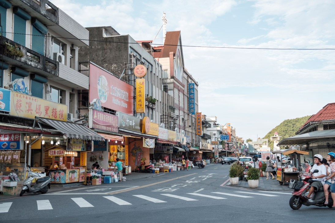 Busy street scene in Yilan, Taiwan with colorful storefronts, Chinese signage, and people on scooters