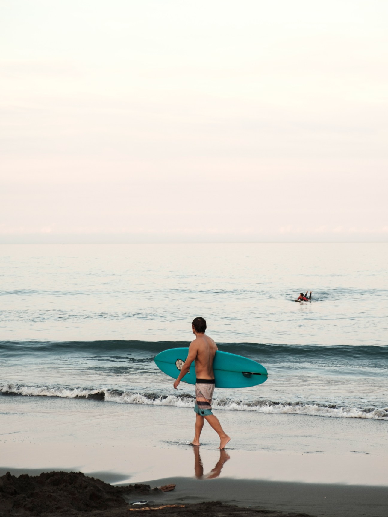 Person carrying turquoise surfboard walking along beach shoreline at Wai'ao Beach