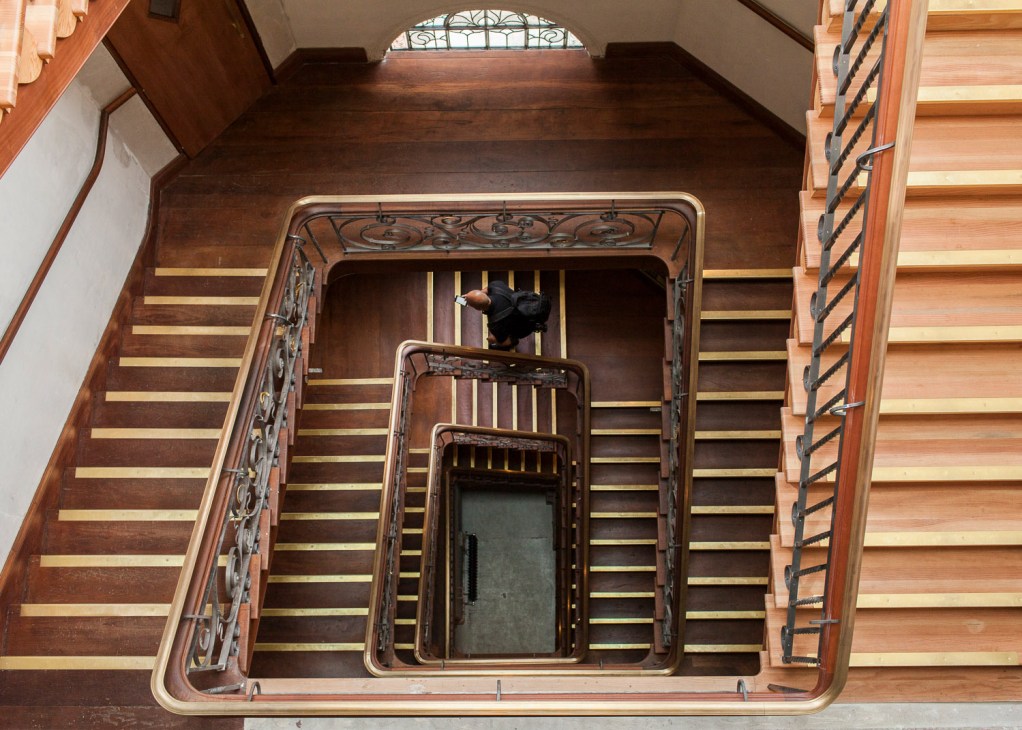 Overhead view of a grand mahogany staircase with brass balustrade and emerald-green tiling in Squire and Partners' headquarters.