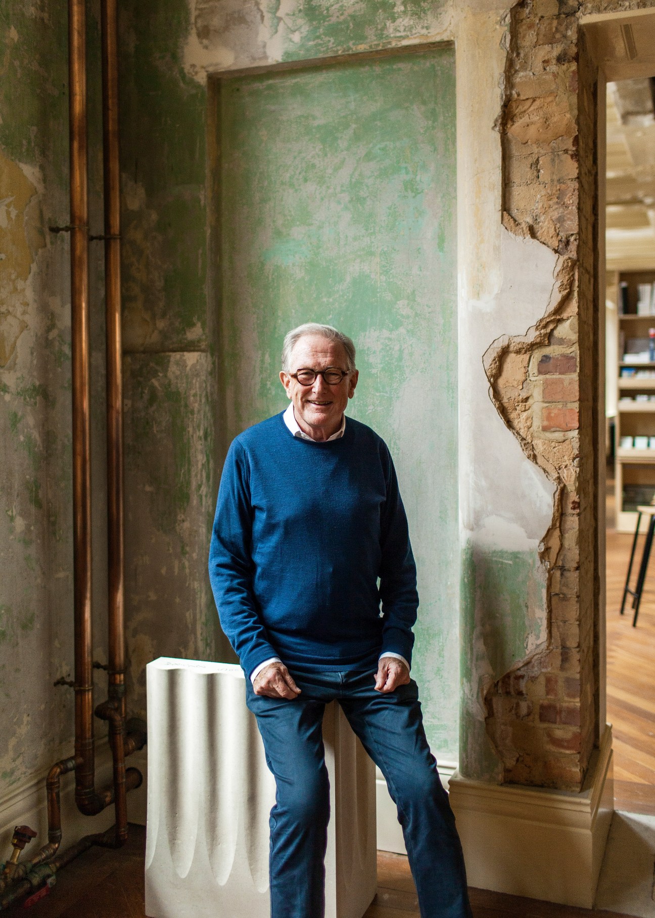 Michael Squire, co-founder of Squire and Partners, poses in a corridor with exposed weathered walls.
