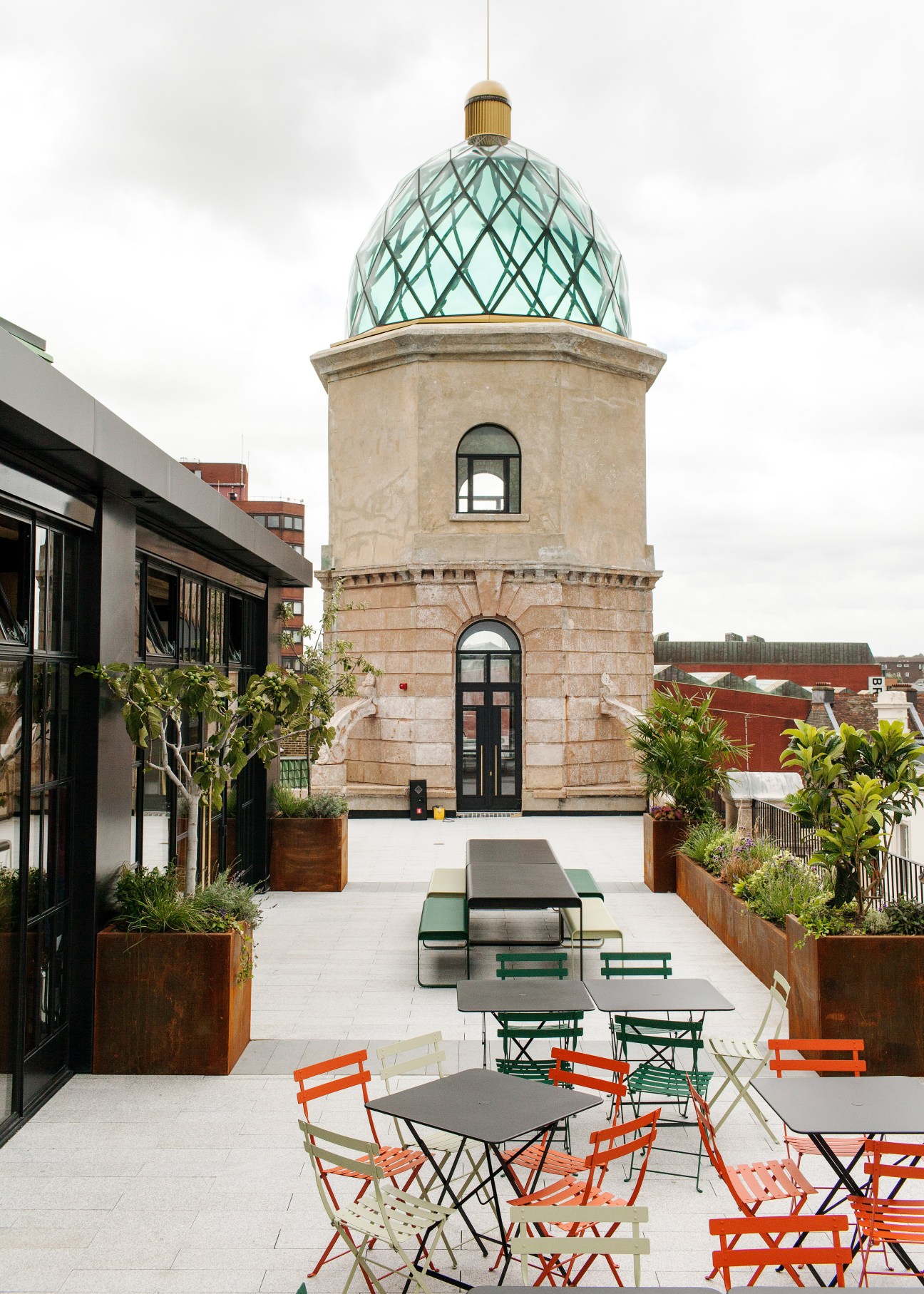 Rooftop terrace with colorful chairs and tables beneath a custom glass dome with green lattice pattern.