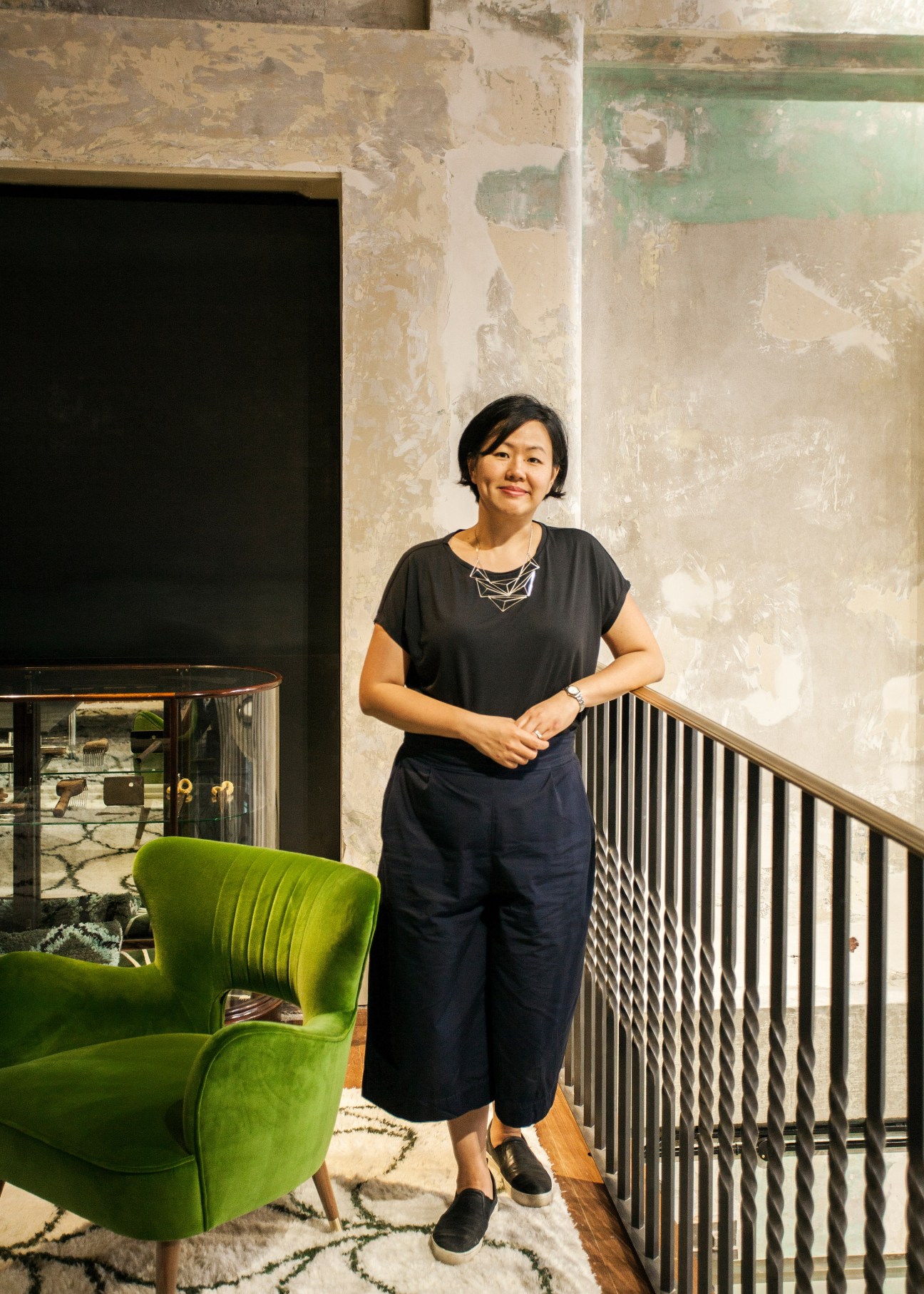 Maria Cheung, director of interiors, standing in The Department Store office space with exposed weathered walls and green chair.