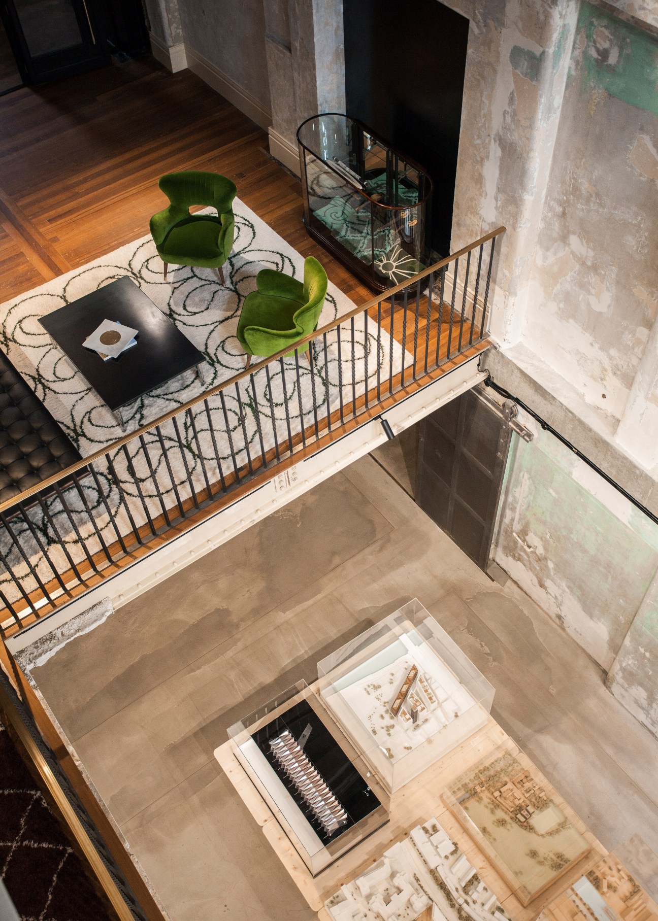 Overhead view of a mezzanine level with green chairs, patterned rug, black table, and exposed architectural elements in a renovated building interior.