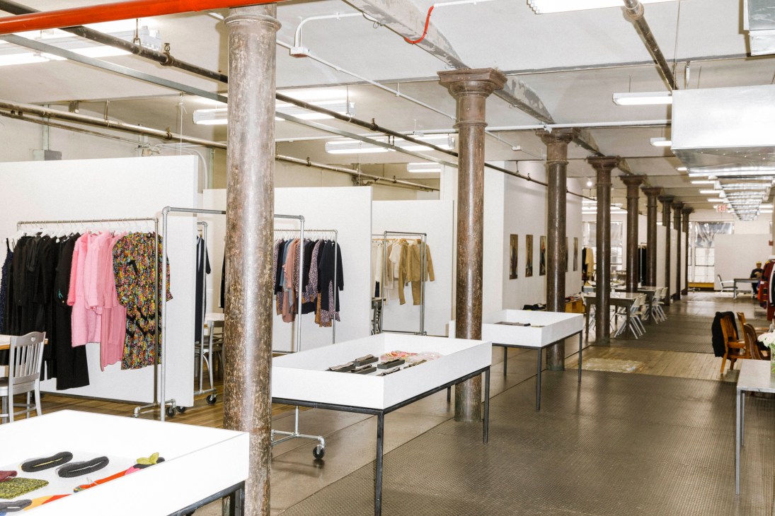 Industrial loft showroom with clothing racks, white tables, exposed columns and fluorescent lighting